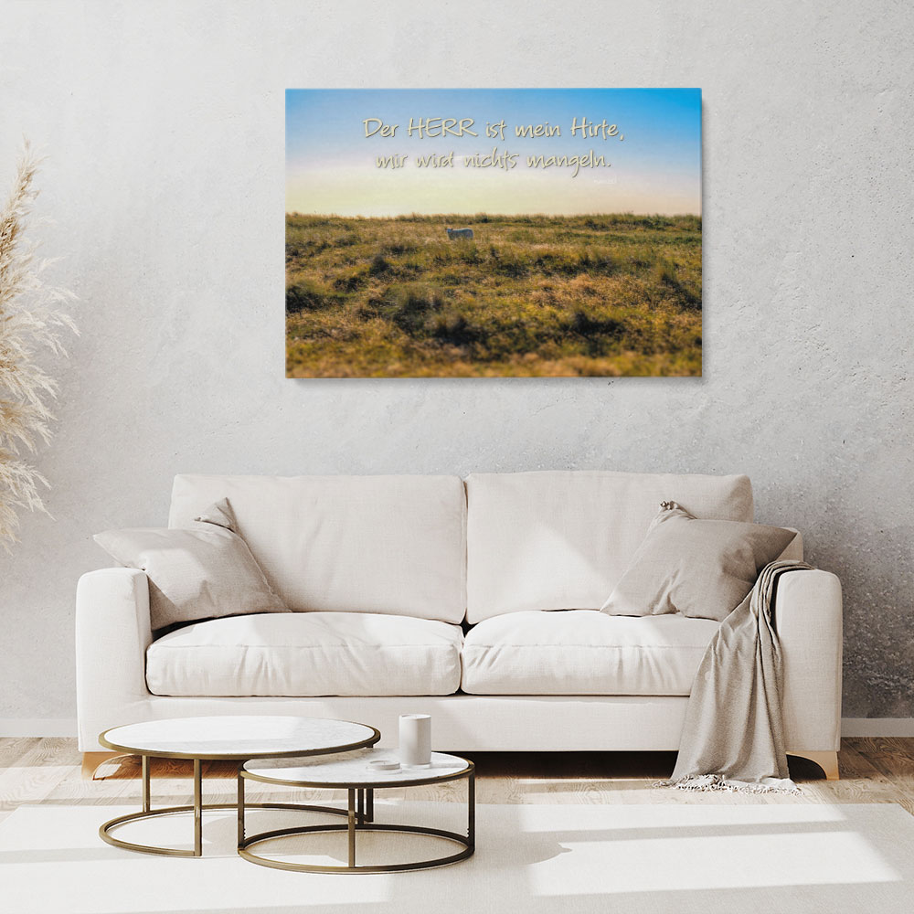 Mockup eines christlichen Leinwandbildes mit Schaf in weiter Landschaft und dem Bibelvers Der HERR ist mein Hirte über einem hellen Sofa im Wohnzimmer