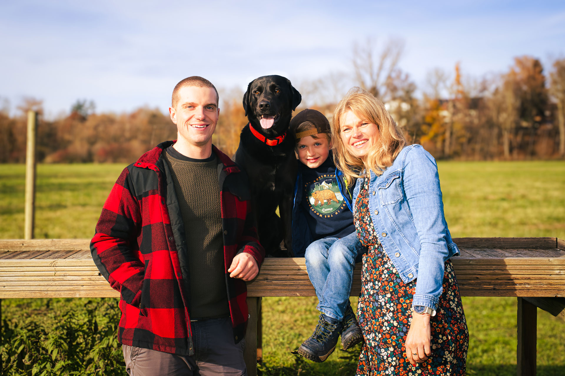 Familie mit Kind und schwarzem Hund bei einem natürlichen Outdoor-Fotoshooting auf dem Land in warmem Sonnenlicht