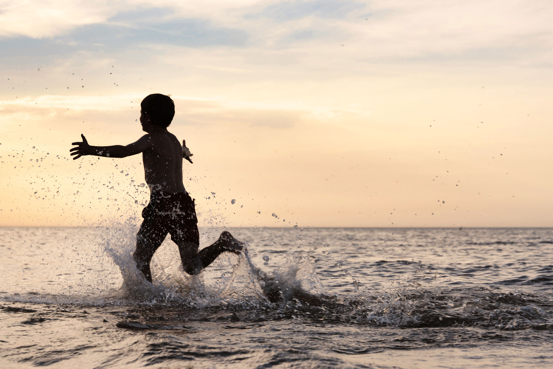Kind im Meer bei Sonnenuntergang Silhouette eines Kindes, das bei Sonnenuntergang spielend durch flaches Meerwasser läuft