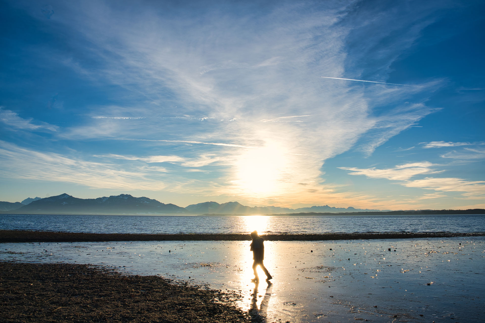 Kind am Ufer bei Sonnenuntergang mit Bergpanorama Silhouette eines Kindes am Wasser bei Sonnenuntergang vor Bergpanorama und weitem Himmel