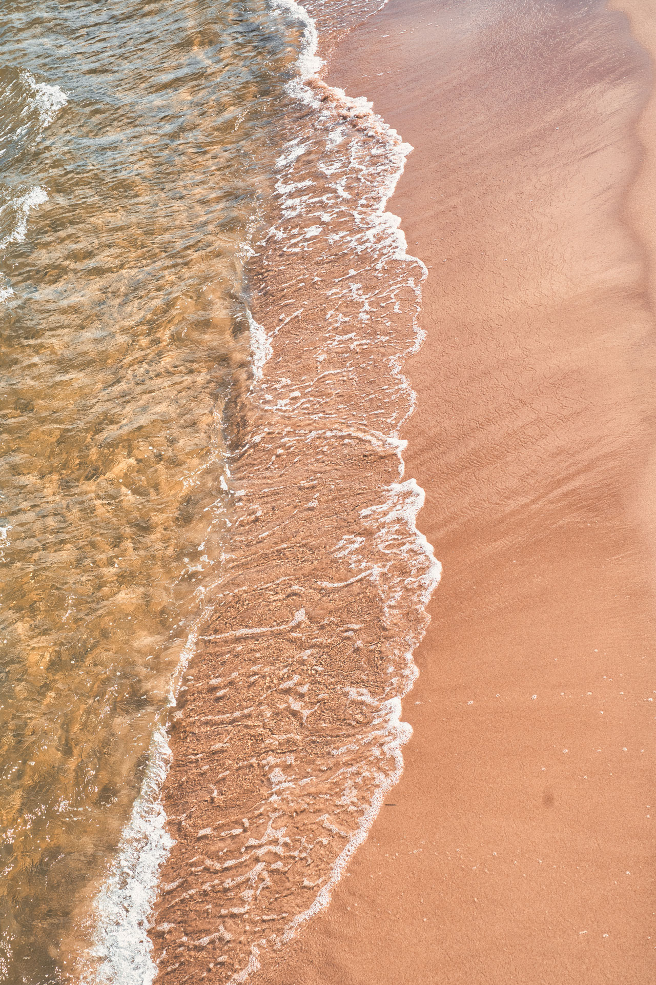 Sanfte Wellen am Sandstrand Sanfte Wellen laufen über einen warmen Sandstrand mit feiner Schaumkante