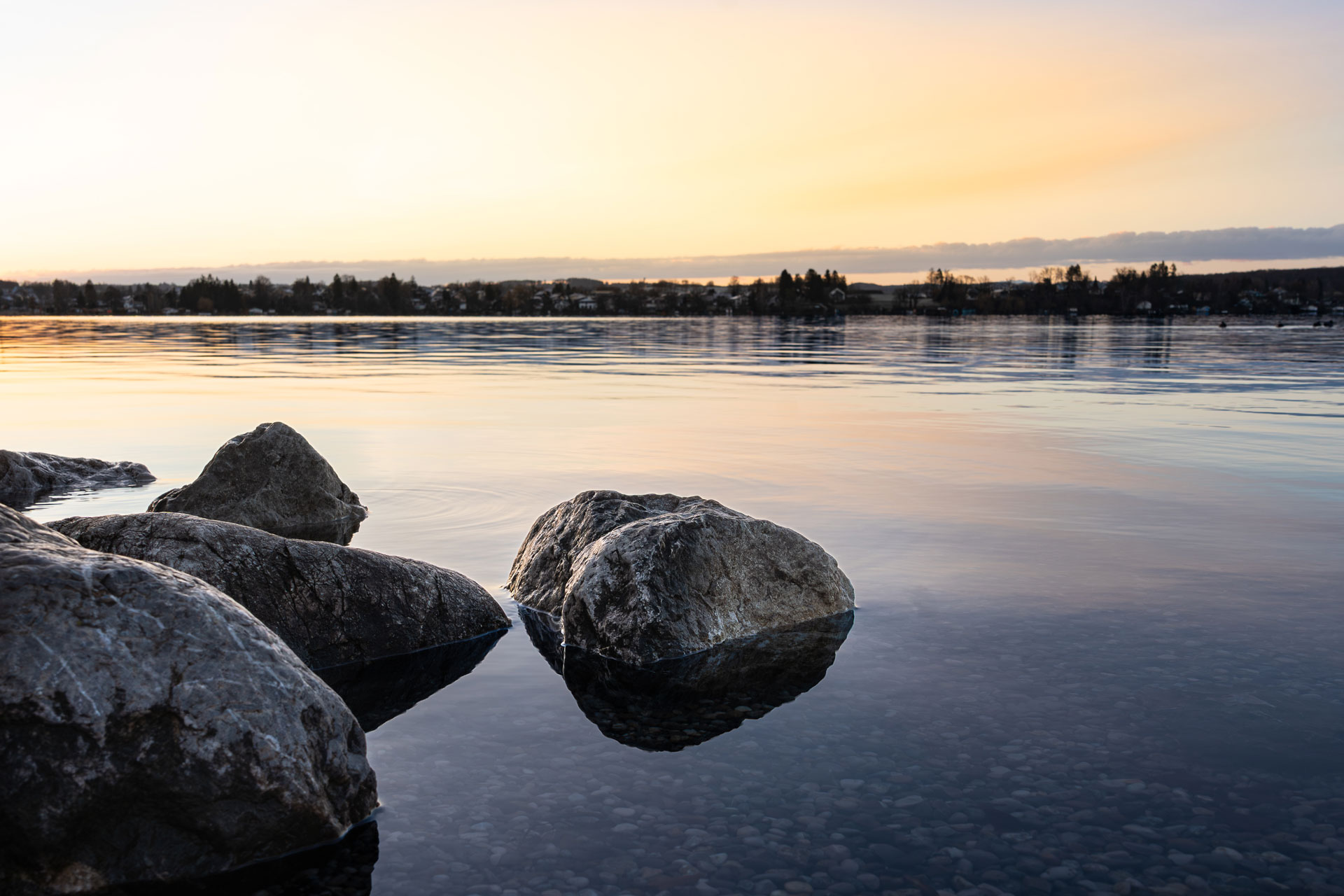 Ruhige Uferlandschaft am Wörthsee bei Sonnenaufgang mit Steinen im klaren Wasser und sanften Spiegelungen